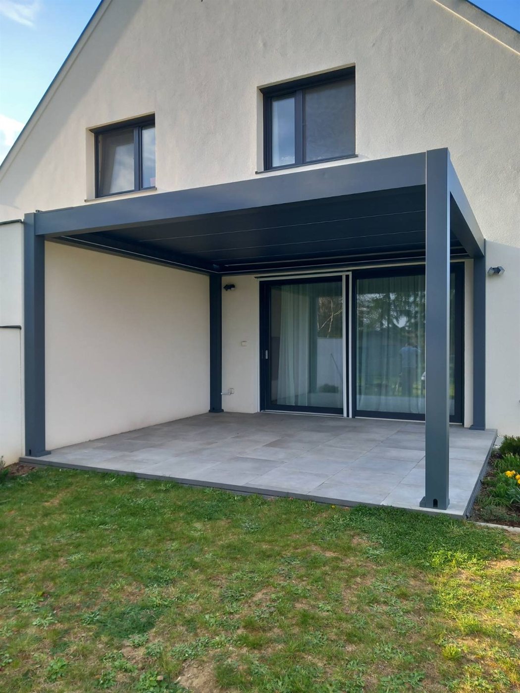 Antracit alumínium pergola családi házhoz építve, nappali fényben