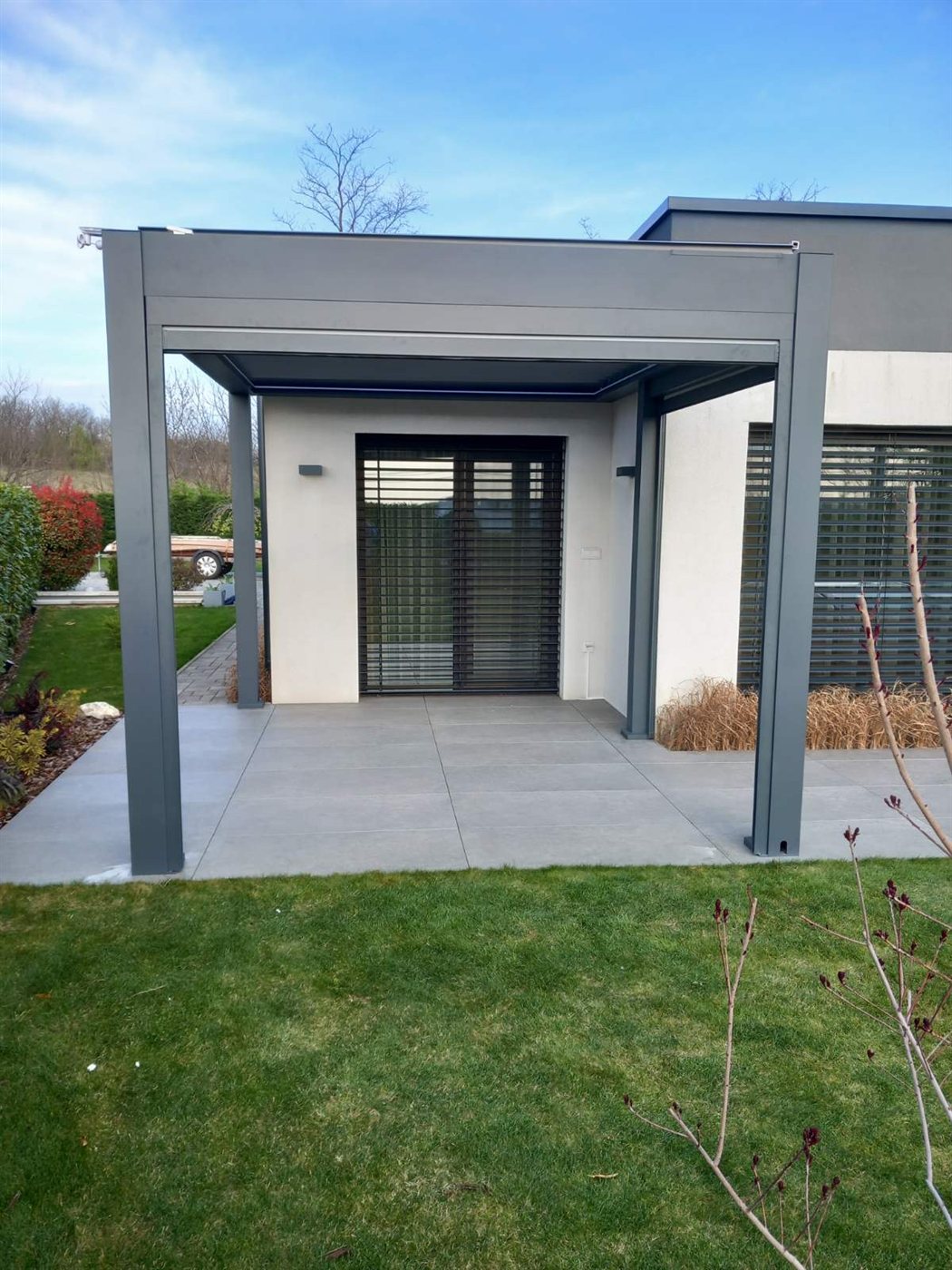 Szabadon álló antracit pergola modern ház teraszán, kék ég alatt