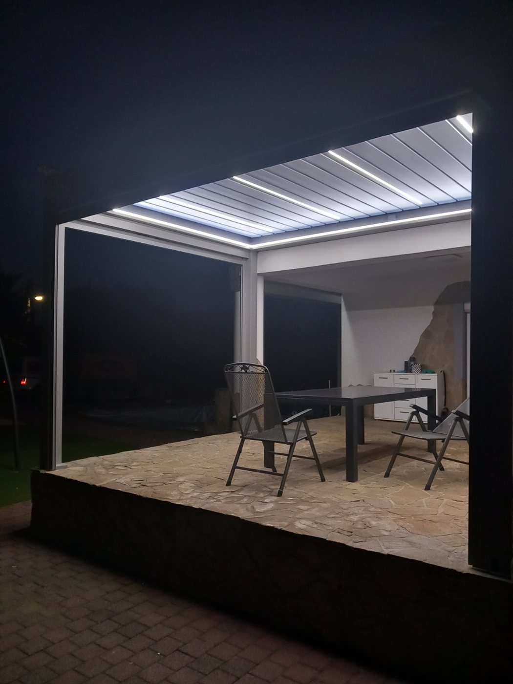 Pergola fehér lamellavilágítással, esti étkezősarok a teraszon